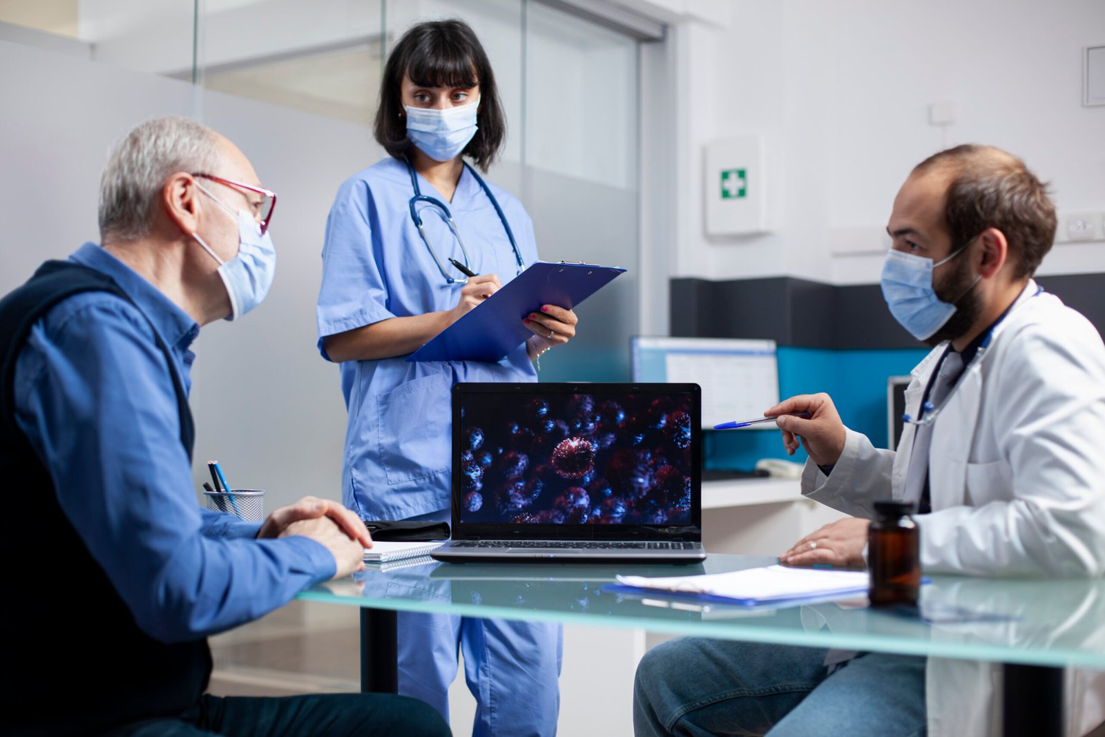 Doctor and old patient analyze digital display of microscopic germs as female nurse writes notes on clipboard. Healthcare workers discuss disease prevention and treatment with senior man in clinic.